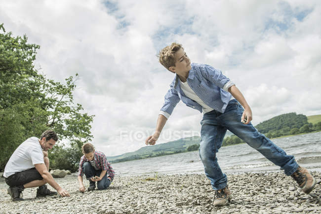 Homme et deux garçons écrémage pierres — Photo de stock
