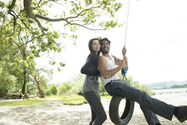Hombre y mujer jugando con neumáticos colgados de un árbol - foto de stock