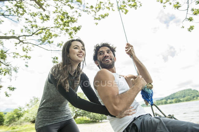 Mann und Frau spielen auf Reifen, die an Baum hängen — Stockfoto