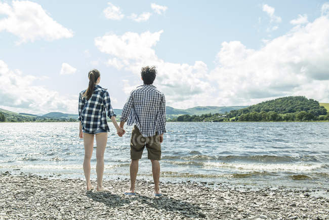 Man and woman standing holding hands on shore — Stock Photo