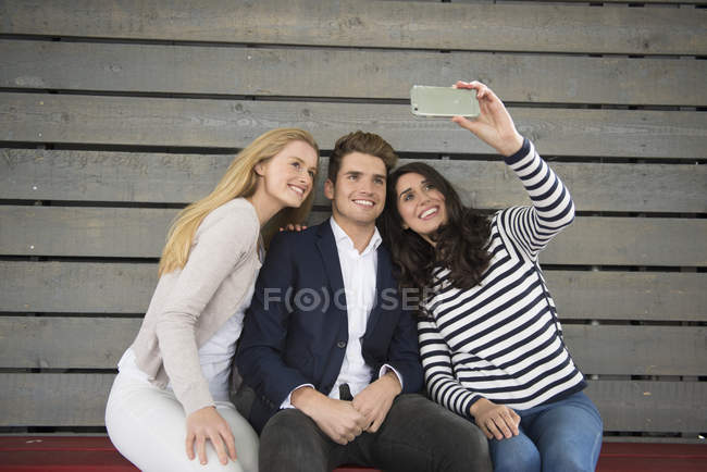 Friends sitting on bench taking selfie — Stock Photo