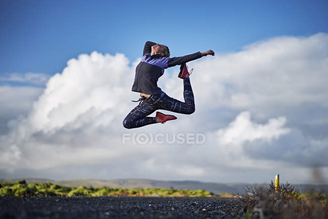Woman leaping by deserted unmade road — Stock Photo