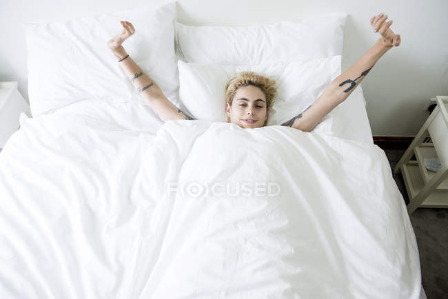 Femme couchée dans son lit étirant les bras — Photo de stock