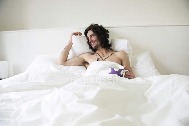 Человек, лежащий в постели с чашкой чая — стоковое фото