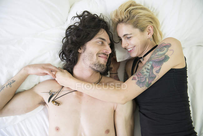 Couple tatoué câlins sur le lit — Photo de stock