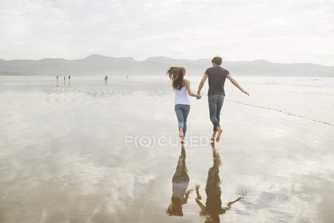 Пара бежит, держа руки на пляже — стоковое фото