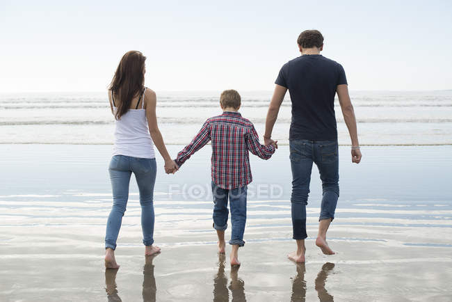 Пара и сын, гуляющие в лучах солнца на пляже — стоковое фото