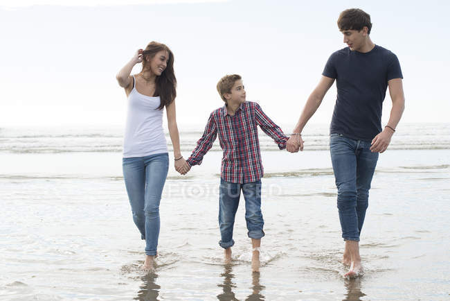 Пара и сын, гуляющие в лучах солнца на пляже — стоковое фото