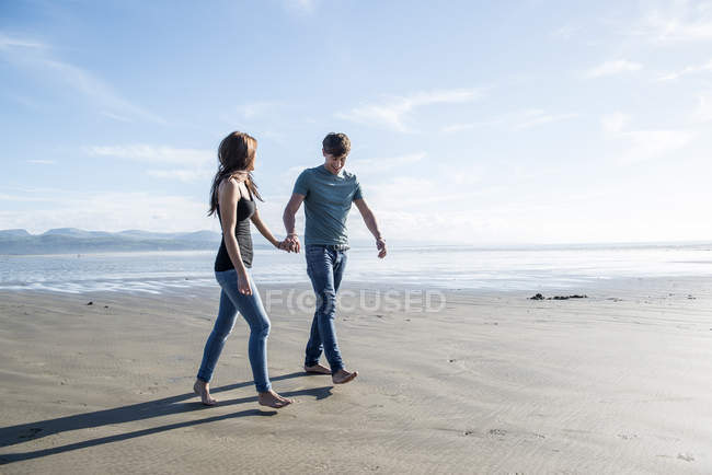 Couple walk holding hands across beach — Stock Photo