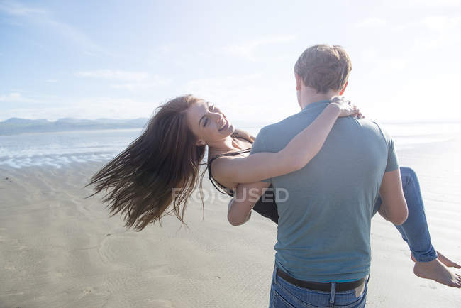 Мужчина, несущий партнера через пляж — стоковое фото
