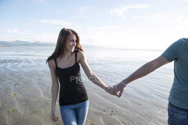 Coppia camminare tenendosi per mano attraverso la spiaggia — Foto stock