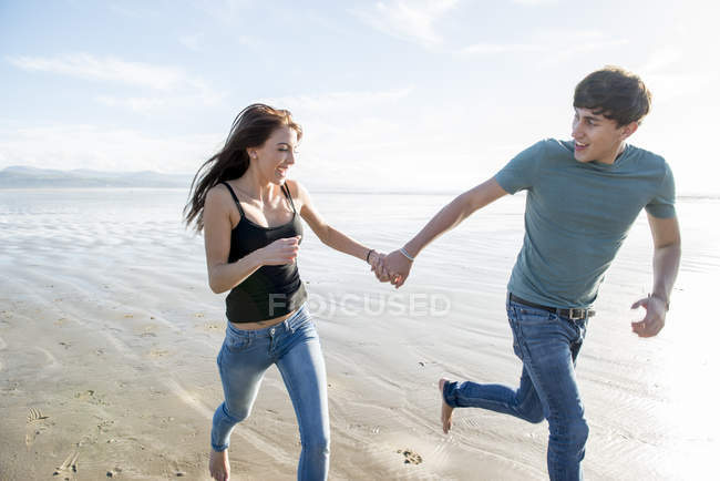 Couple running whilst holding hands on beach — Stock Photo