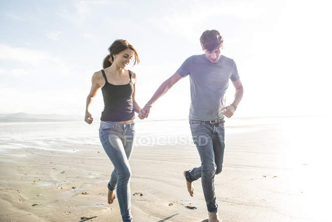 Pareja corriendo mientras toma de la mano en la playa - foto de stock