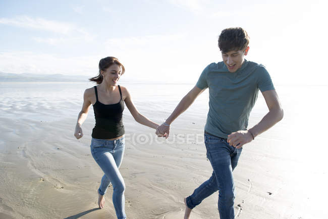 Coppia correre mentre si tiene per mano sulla spiaggia — Foto stock