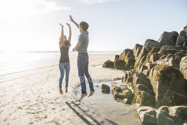 Пара, прыгающая в лучах солнца на пляже — стоковое фото