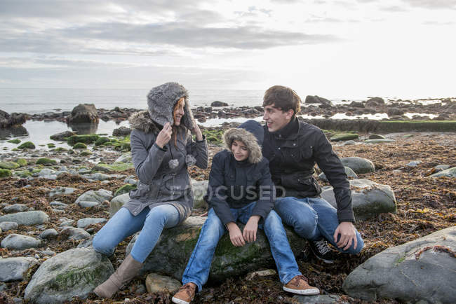 Pareja e hijo disfrutando sentado en roca - foto de stock