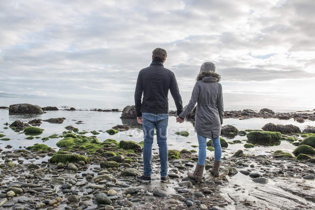 Casal de pé, mantendo as mãos na praia — Fotografia de Stock