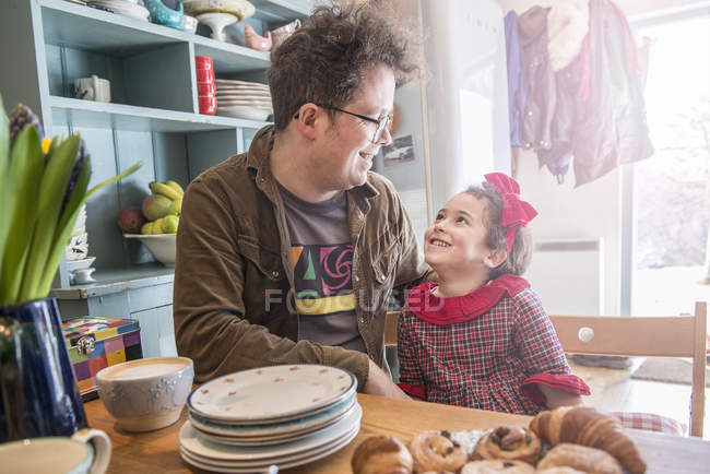 Padre se sienta en la cocina charlando con su hija - foto de stock