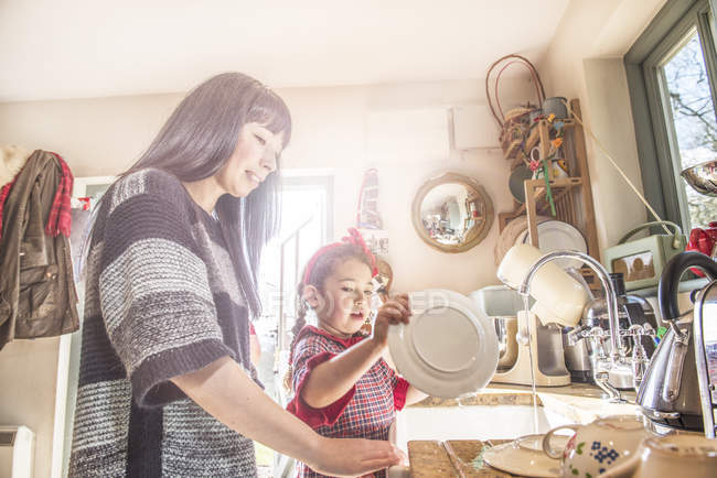 Chica con la madre lavando platos - foto de stock