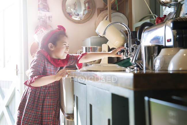 Chica lavando platos en fregadero de cocina - foto de stock