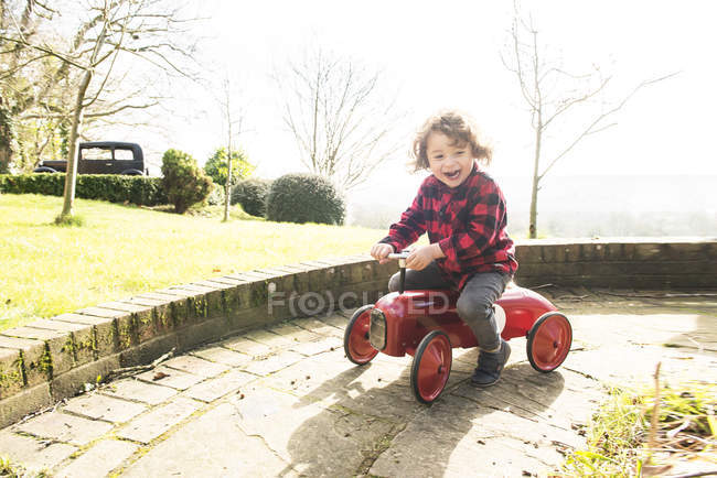 Niño montar juguete tractor alrededor de jardín - foto de stock