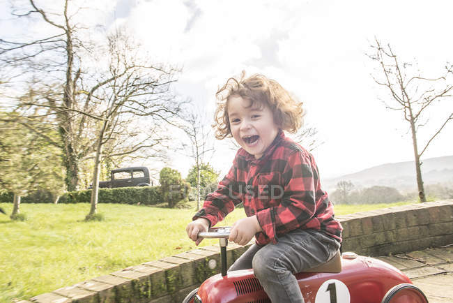 Мальчик катается на игрушечном тракторе вокруг сада — стоковое фото