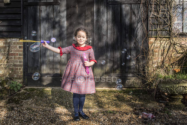 Дівчина дме бульбашки біля гаражних дверей — стокове фото