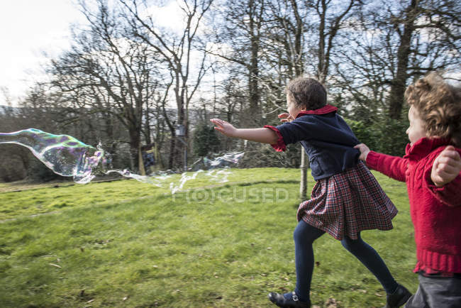 Kinder jagen Blasen durch Garten — Stockfoto