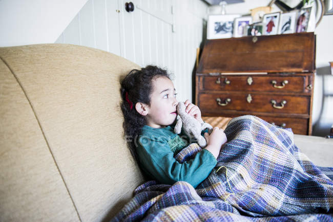 Menina segurando brinquedo coelho sentado no sofá — Fotografia de Stock