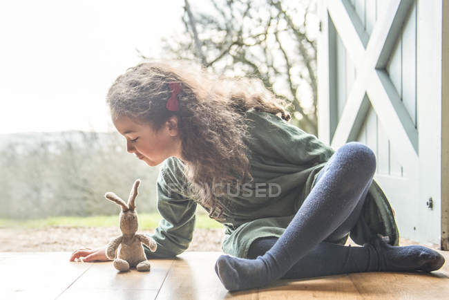 Девушка сидит у задней двери, играет с игрушечным кроликом — стоковое фото