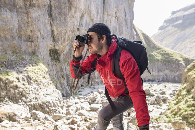 Mountaineer climbing over rocks and taking photographs — Stock Photo