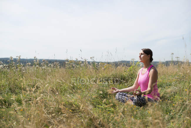Mujer en prado practicando yoga - foto de stock