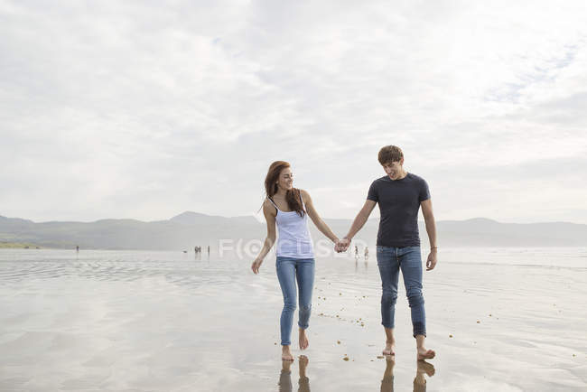 Casal andar de mãos dadas em toda a praia — Fotografia de Stock
