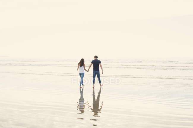 Couple walk holding hands across beach — Stock Photo