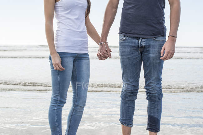 Пара, стоящая на пляже и держащаяся за руки — стоковое фото