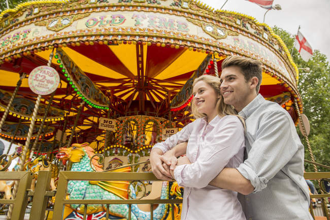 Couple cuddling in front of carousel — Stock Photo