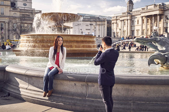 Homme photographiant petite amie près de la fontaine — Photo de stock