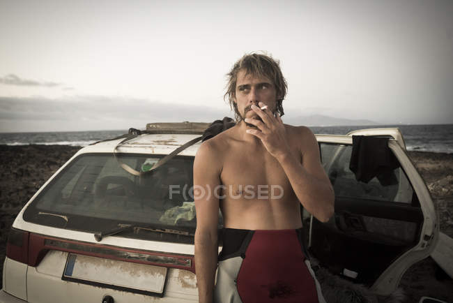 Man in wetsuit smoking cigarette by car — Stock Photo