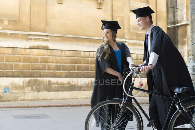 Estudiantes en vestidos de graduación ciclismo a través de terrenos - foto de stock