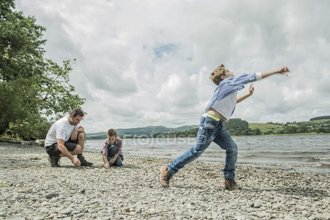 Homem e meninos skimming pedras na costa — Fotografia de Stock