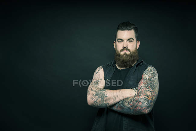 Hombre con brazos tatuados doblados - foto de stock