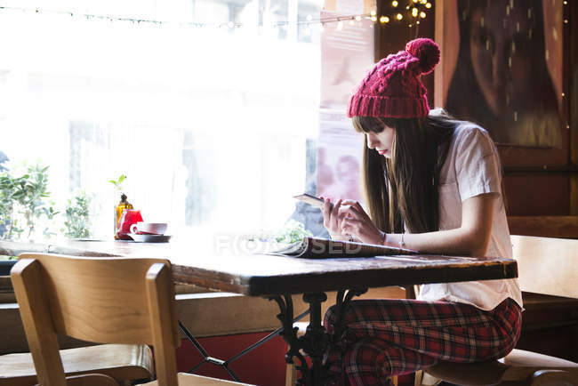 Frau sitzt am Tisch und nutzt Smartphone — Stockfoto