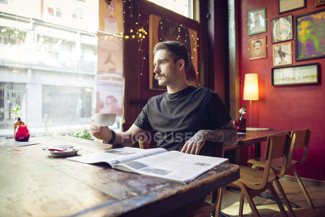 Человек сидит за столом и смотрит в окно — стоковое фото