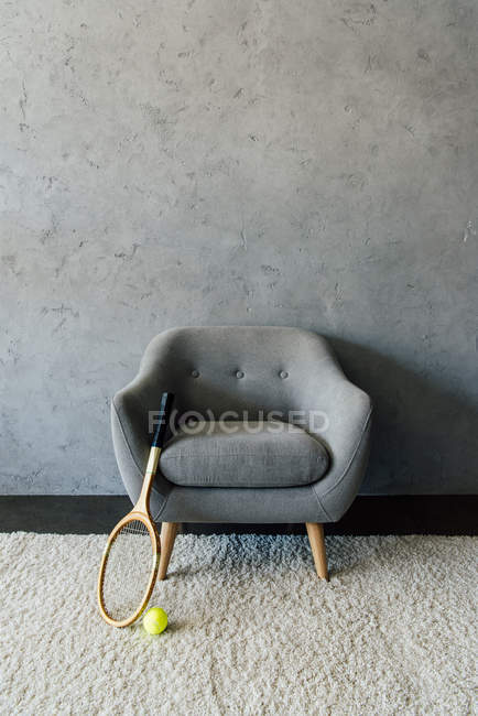 Raqueta de tenis y pelota con sillón gris - foto de stock