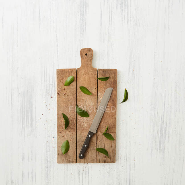 Tábua de corte de madeira, faca e folhas — Fotografia de Stock