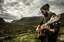 Man playing guitar at Glencoe highland — Stock Photo