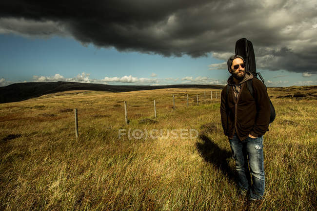 Homme marchant sur prairie avec guitare en sac — Photo de stock
