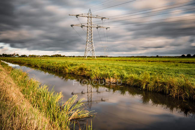 Electric tower in field next to stream — Stock Photo