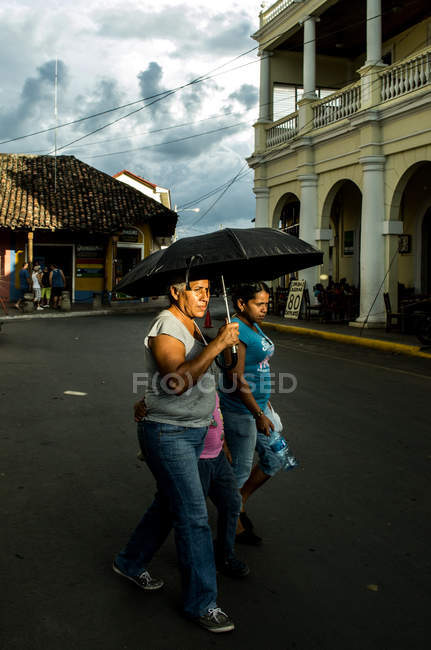 Femmes avec enfant marchant dans la rue avec parapluie — Photo de stock