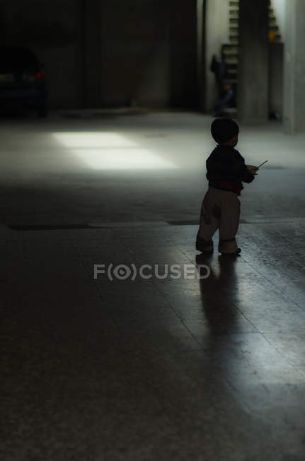 Niño de pie en habitación oscura - foto de stock